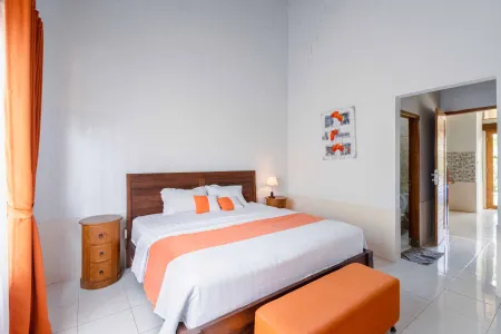 Cozy wooden bed in a bright white-walled Balinese-style bedroom with orange accents and open bathroom door.